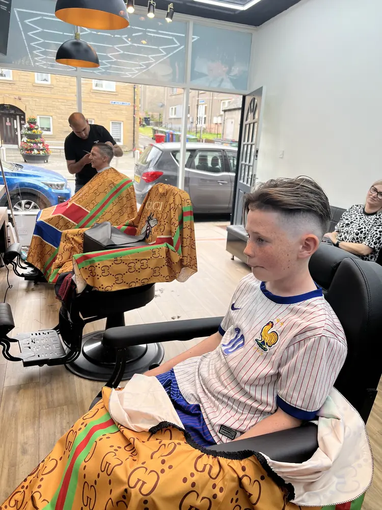 A barber trimming a client while another waits in the next chair